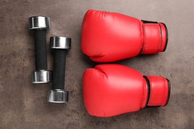 Metal dumbbells and boxing gloves on brown textured table, flat lay