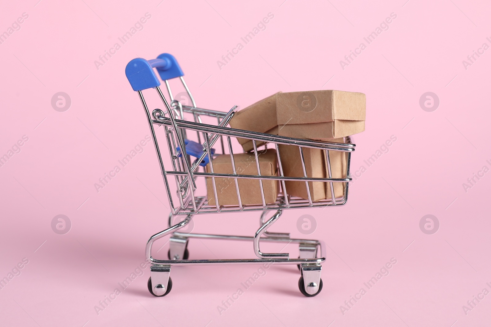 Photo of Small metal shopping cart with cardboard boxes on pink background