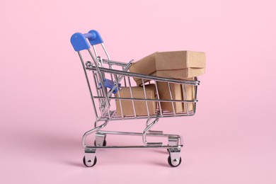 Photo of Small metal shopping cart with cardboard boxes on pink background