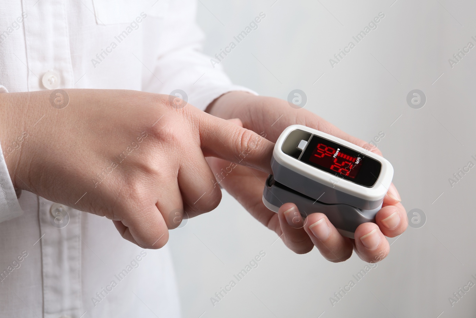 Photo of Woman using modern fingertip pulse oximeter on light background, closeup