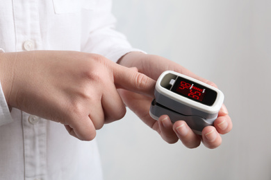 Woman using modern fingertip pulse oximeter on light background, closeup