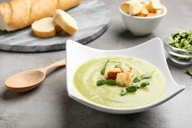 Photo of Bowl of broccoli cream soup with croutons and microgreens served on grey table