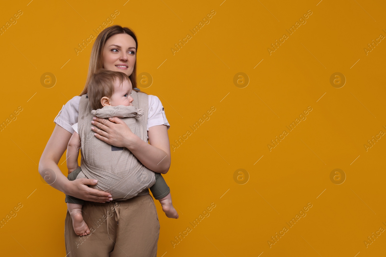 Photo of Mother holding her child in sling (baby carrier) on orange background