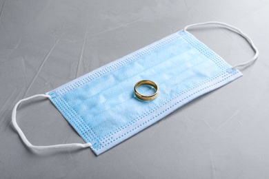 Protective mask and wedding ring on grey table. Divorce during coronavirus quarantine