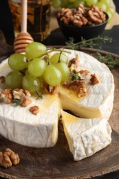 Photo of Brie cheese served with grapes, walnuts and honey on table, closeup
