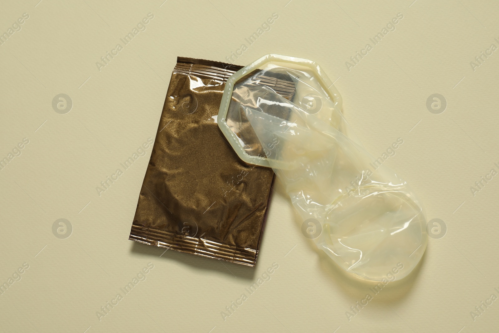 Photo of Unrolled female condom and package on beige background, above view. Safe sex