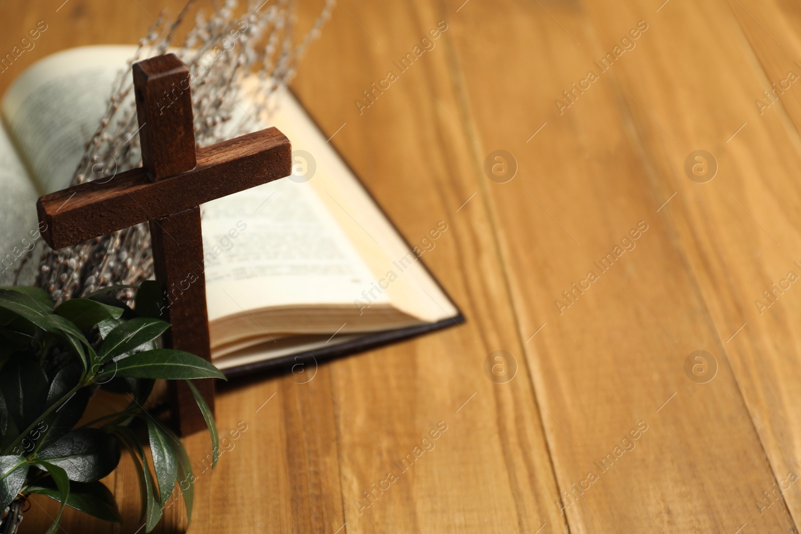 Photo of Cross, Bible and willow branches on wooden table, space for text