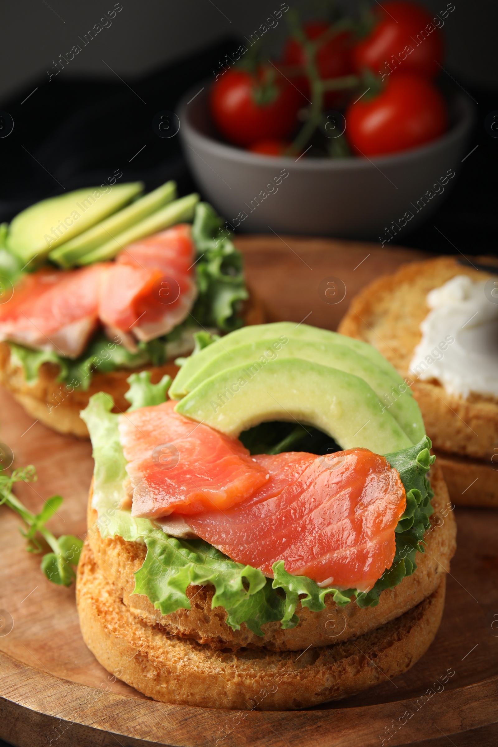 Photo of organic rusks with salmon, cream cheese and avocado served on wooden board, closeup