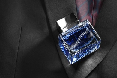 Photo of Luxury men's perfume in bottle on black jacket, space for text