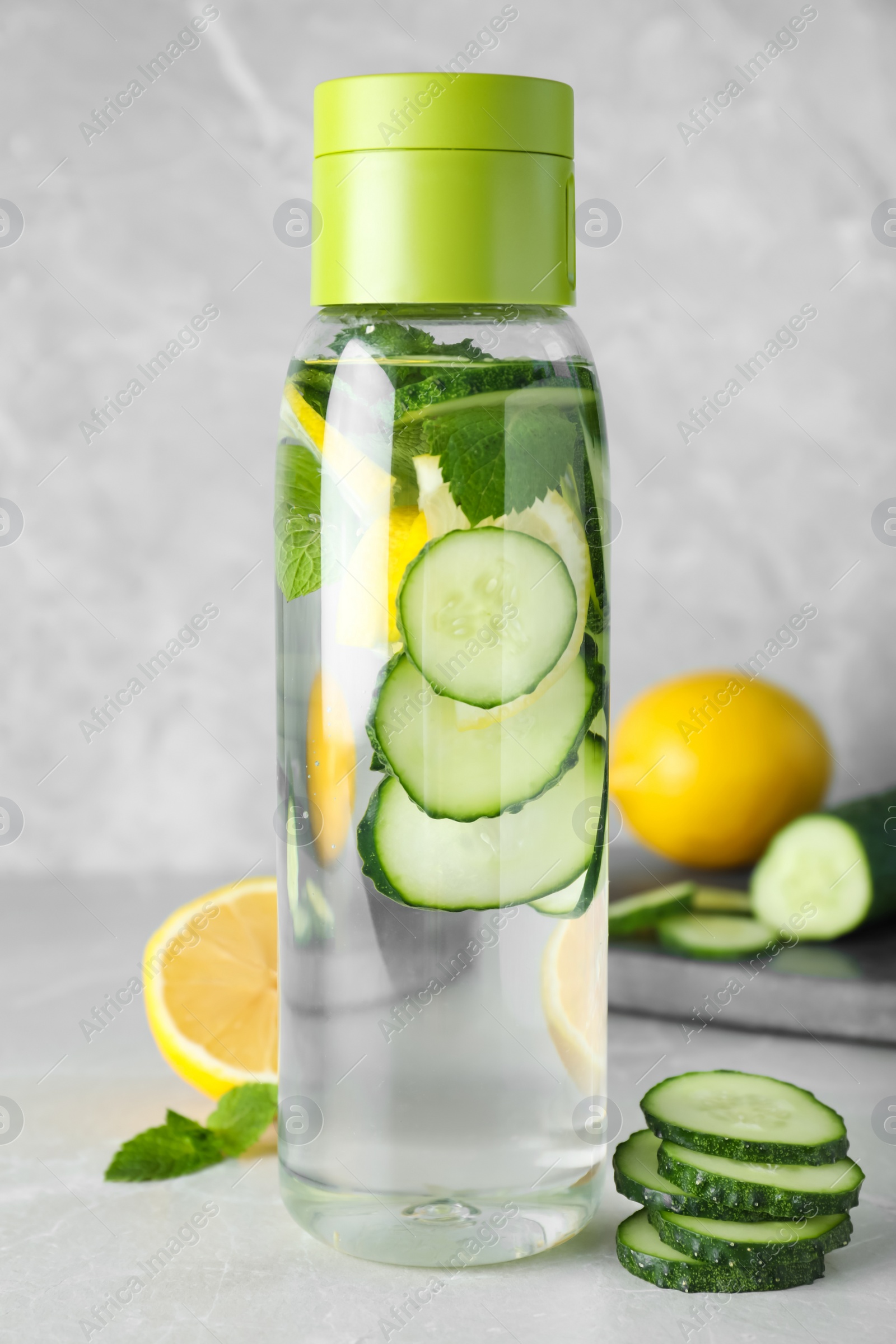 Photo of Bottle of refreshing water with cucumber, lemon and mint on light grey table