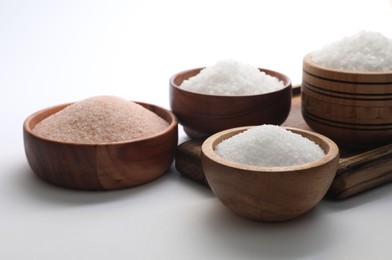 Different types of natural salt in wooden bowls on white background