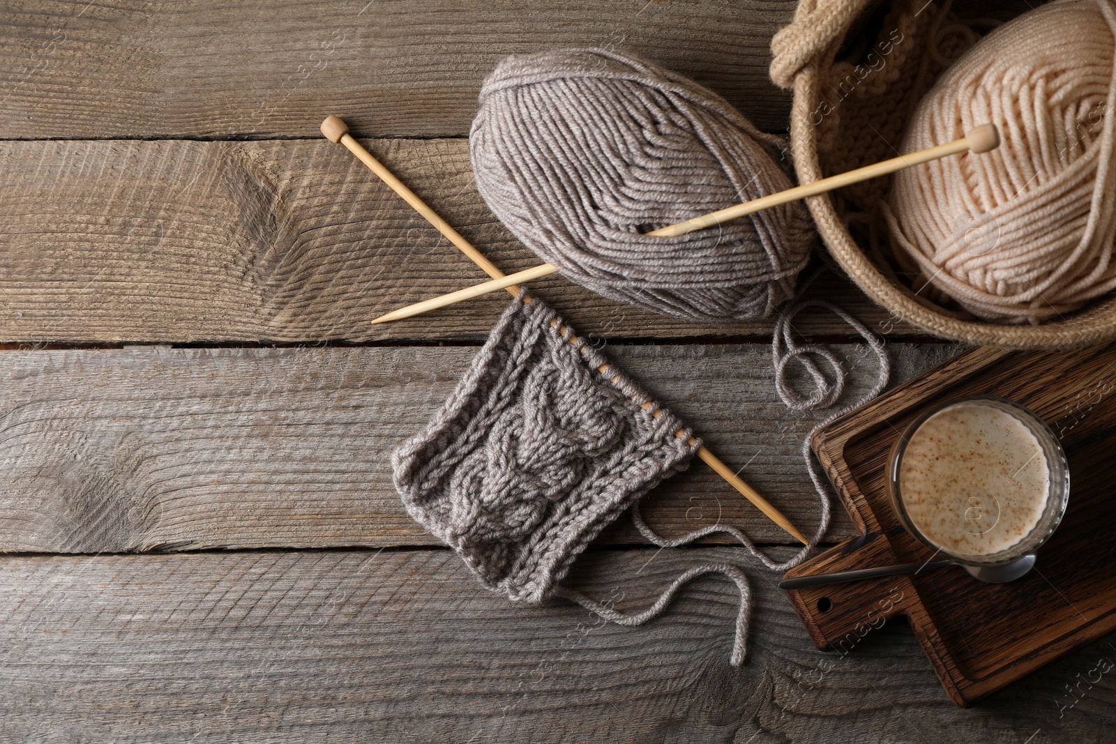 Photo of Soft colorful woolen yarn, knitting, needles and glass of coffee on wooden table, flat lay. Space for text