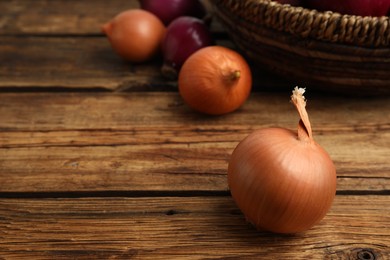 Photo of Onion bulbs and basket on wooden table. Space for text