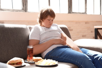 Overweight boy with fast food on sofa at home