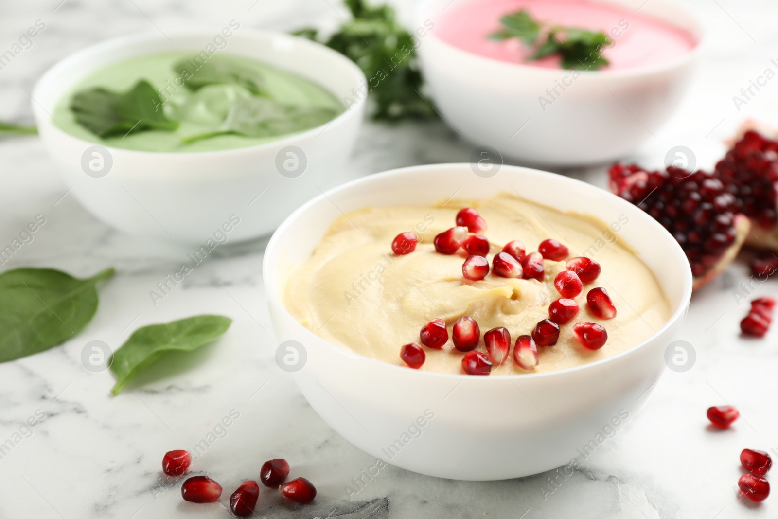 Photo of Bowl of delicious classic hummus with pomegranate seeds on white marble table