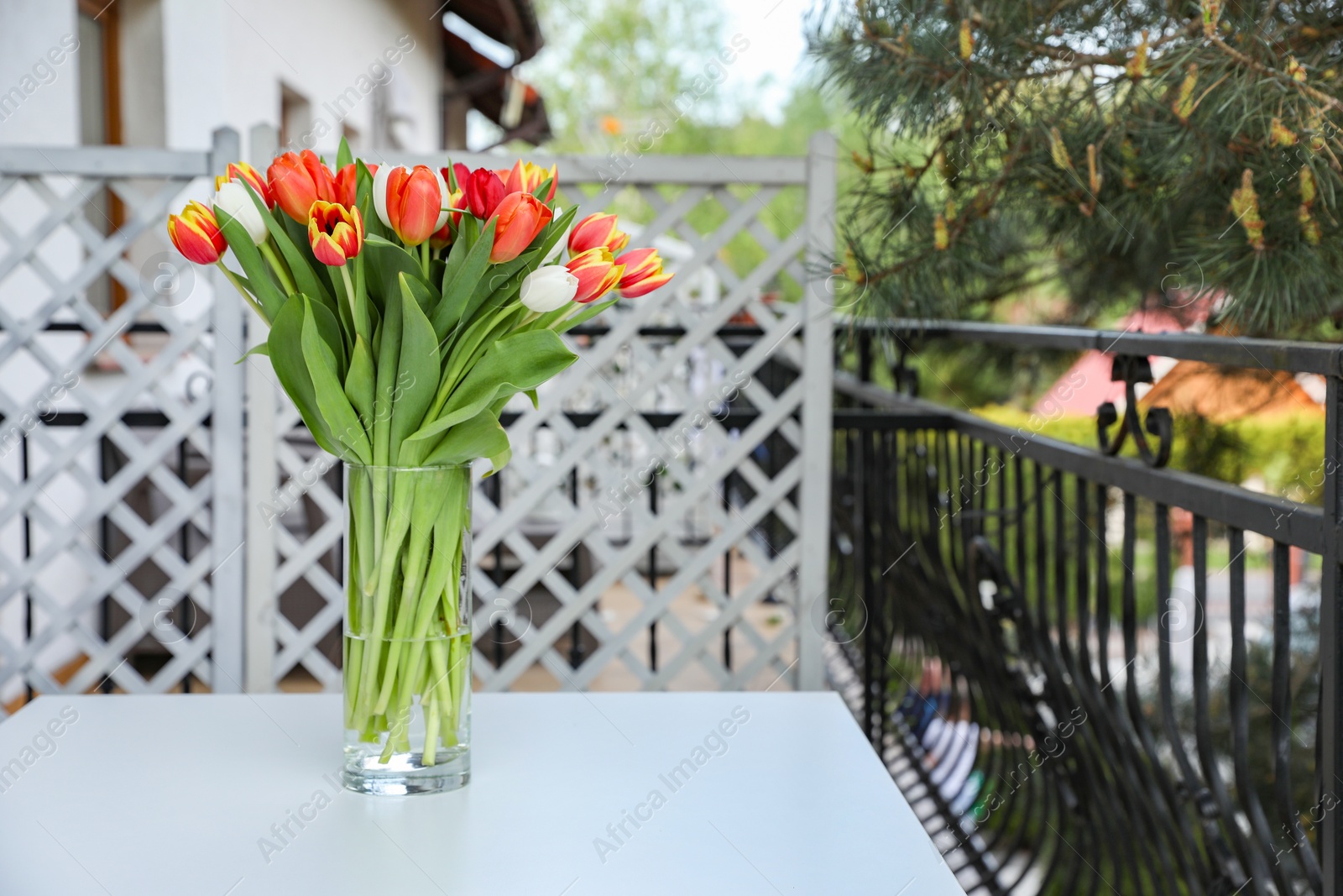 Photo of Beautiful colorful tulips in glass vase on white table at balcony, space for text