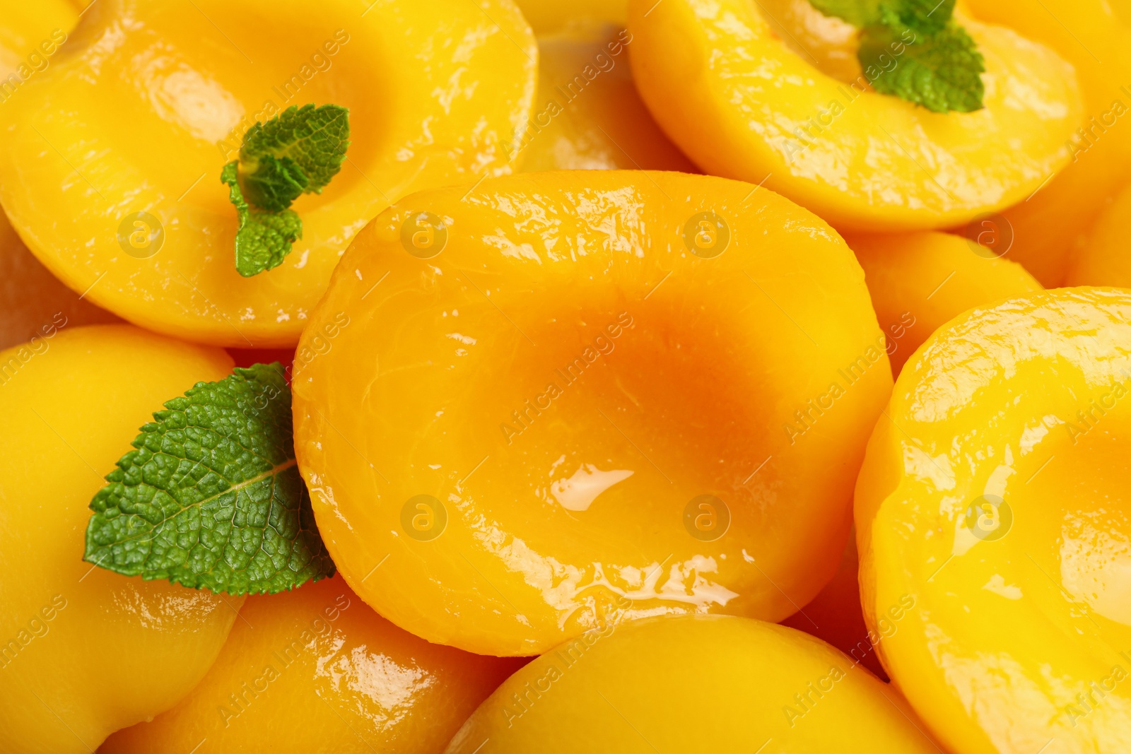 Photo of Halves of canned peaches with mint leaves as background, closeup