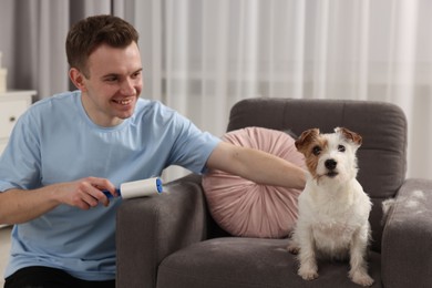 Photo of Smiling man removing pet's hair from armchair at home