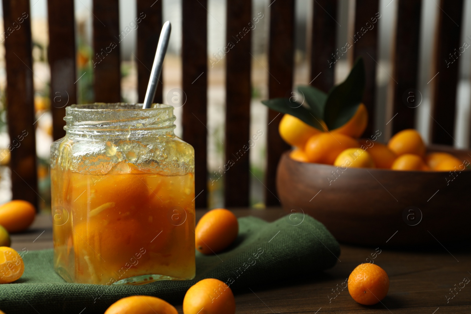 Photo of Delicious kumquat jam in jar and fresh fruits on wooden table, space for text