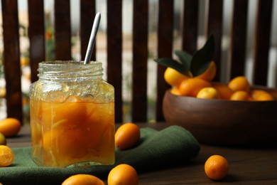 Photo of Delicious kumquat jam in jar and fresh fruits on wooden table, space for text