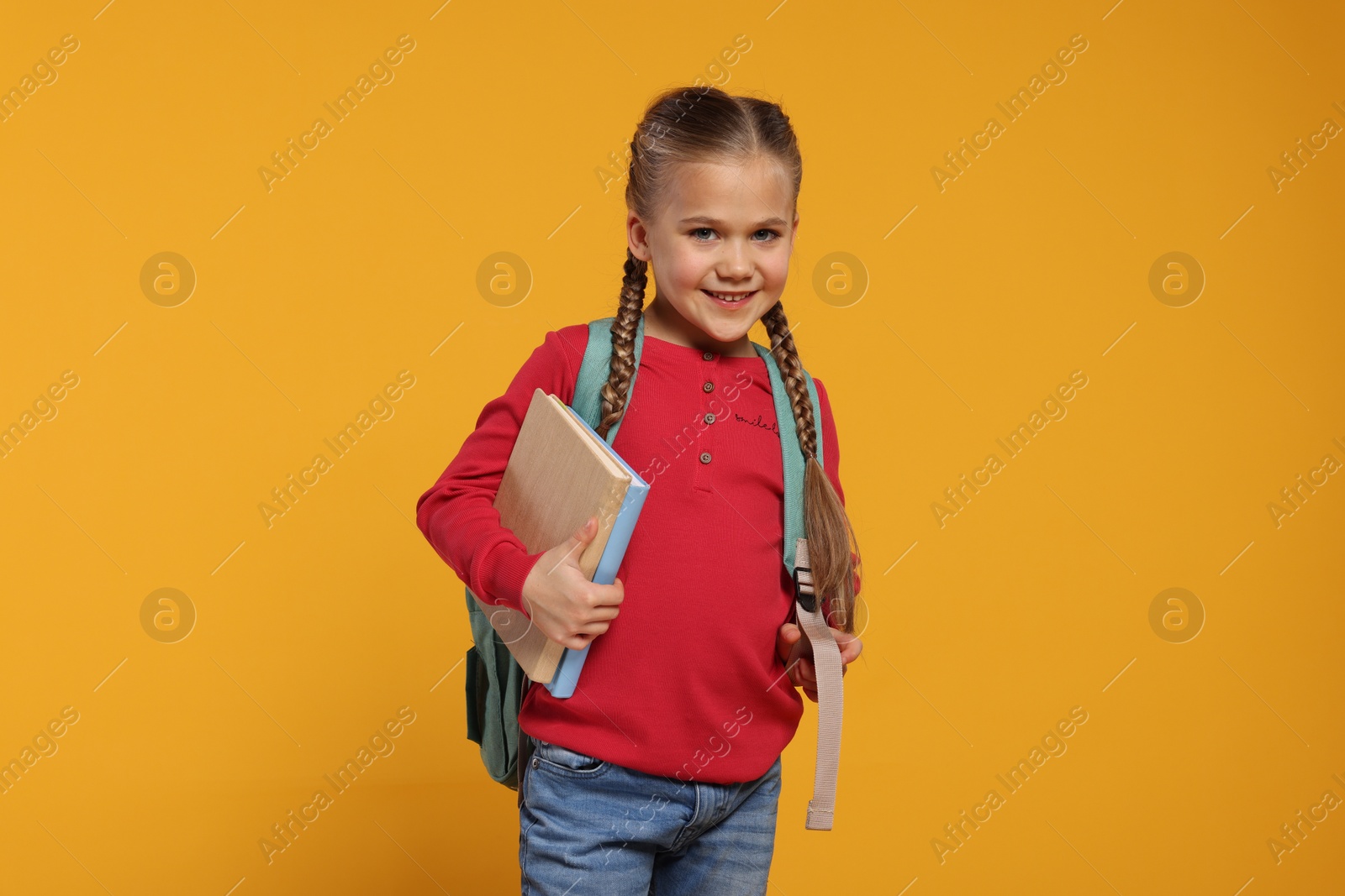 Photo of Happy schoolgirl with backpack and books on orange background