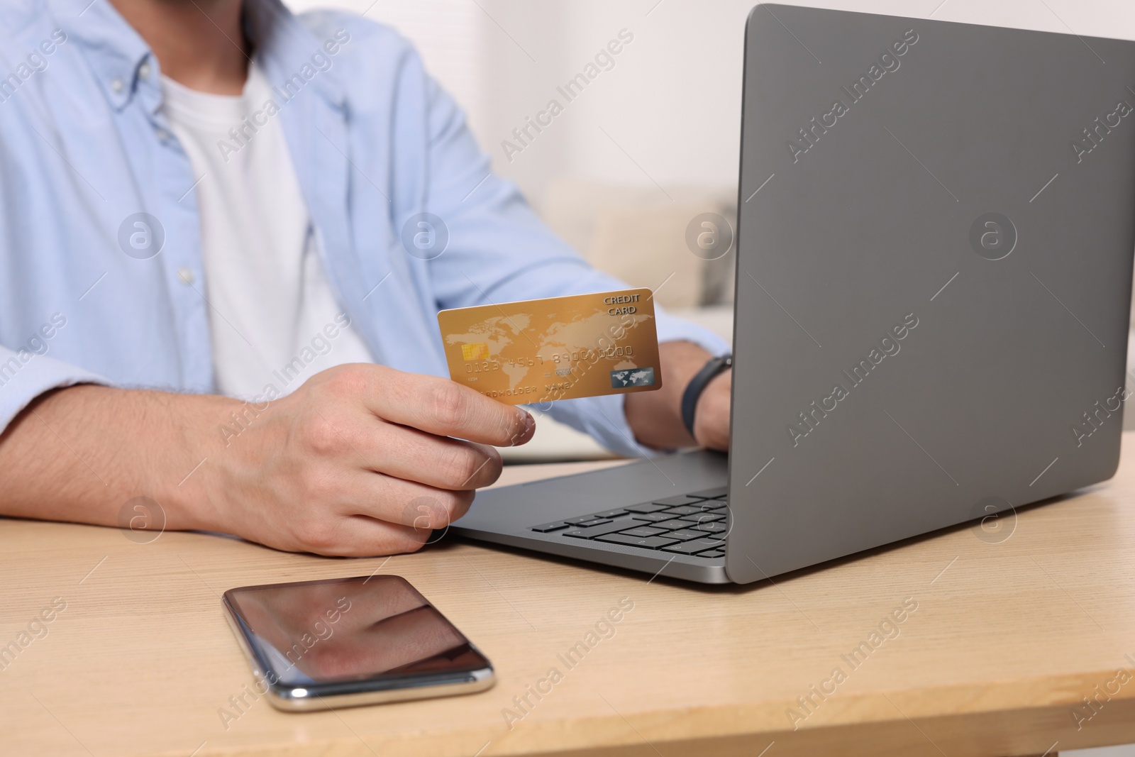 Photo of Man with credit card using laptop for online shopping at wooden table indoors, closeup