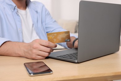 Man with credit card using laptop for online shopping at wooden table indoors, closeup