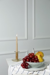 Fresh ripe fruits and burning candle on table indoors