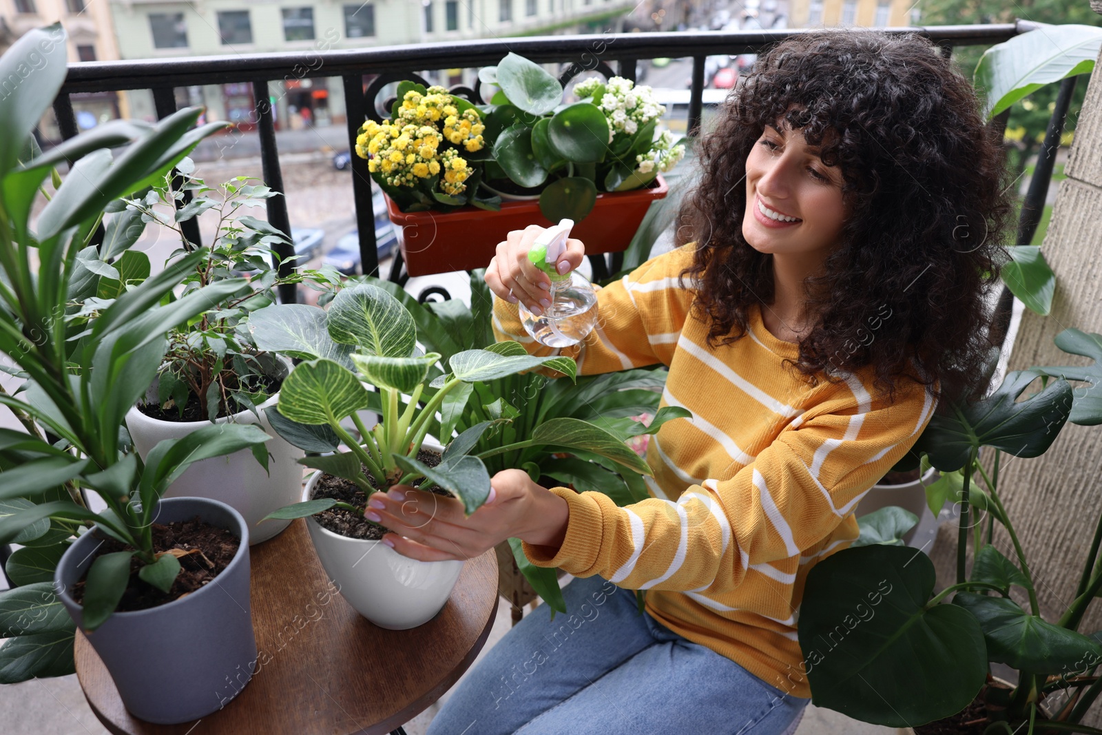 Photo of Beautiful young woman spraying potted houseplants with water on balcony