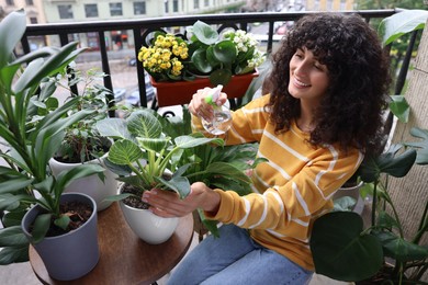 Beautiful young woman spraying potted houseplants with water on balcony