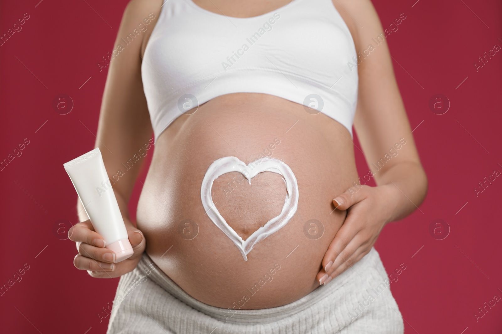 Photo of Young pregnant woman with cosmetic product on pink background, closeup