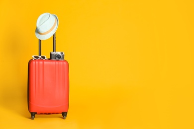 Photo of Travel suitcase with hat, camera and sunglasses on yellow background, space for text. Summer vacation