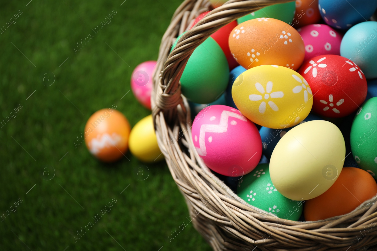 Photo of Colorful Easter eggs in basket on green grass, closeup. Space for text