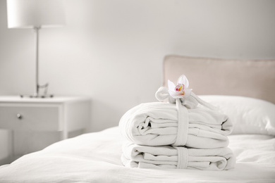 Photo of Clean folded bathrobes on bed in room, space for text