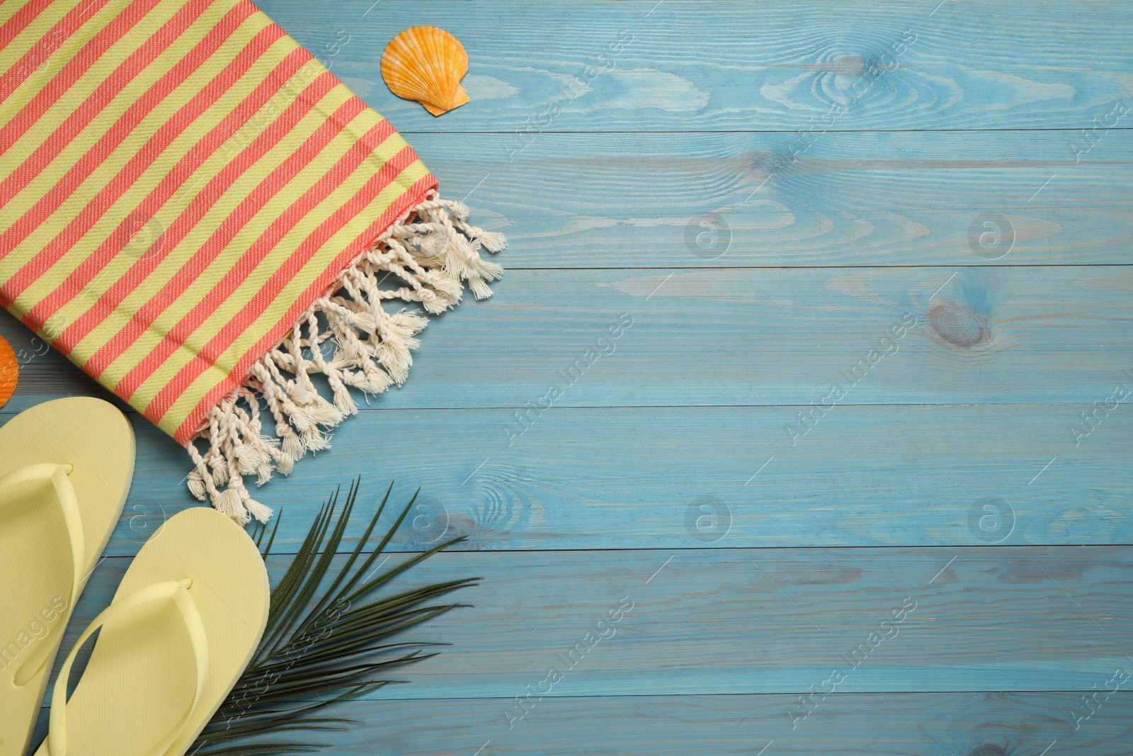 Photo of Beach towel and flip flops on light blue wooden background, flat lay. Space for text