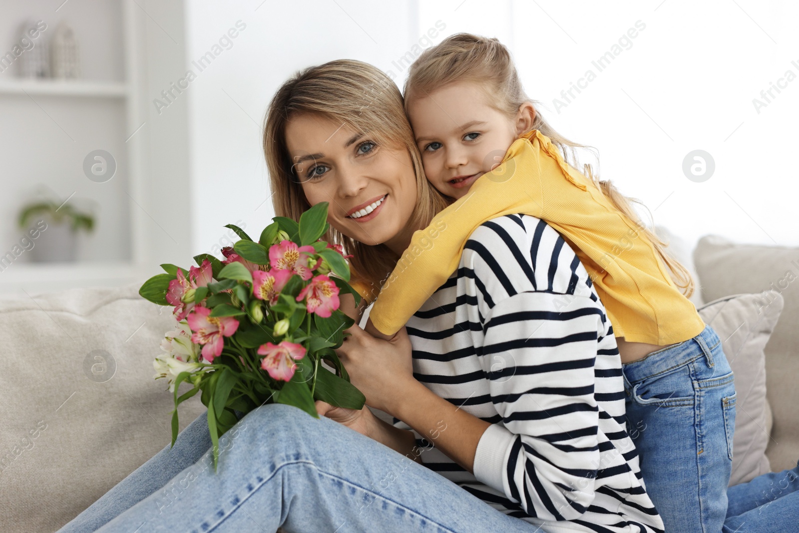 Photo of Little daughter congratulating her mom with Mother`s Day at home. Woman holding bouquet of alstroemeria flowers