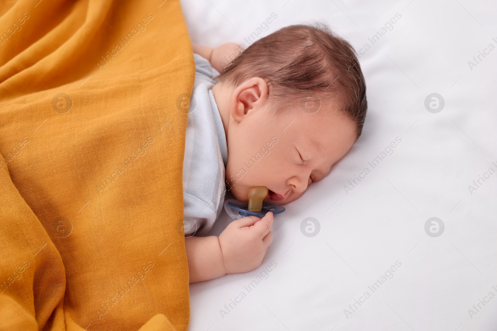 Photo of Cute newborn baby with pacifier sleeping under orange blanket on bed