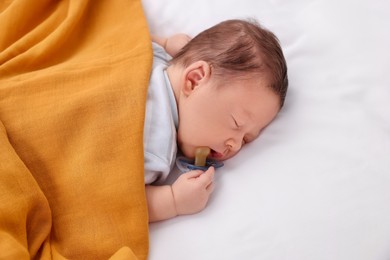 Cute newborn baby with pacifier sleeping under orange blanket on bed