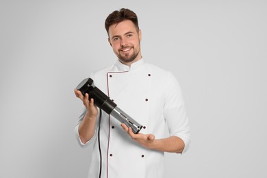 Photo of Smiling chef holding sous vide cooker on beige background