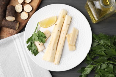 Photo of Cut raw salsify roots with parsley, oil and lemon on grey wooden table, flat lay