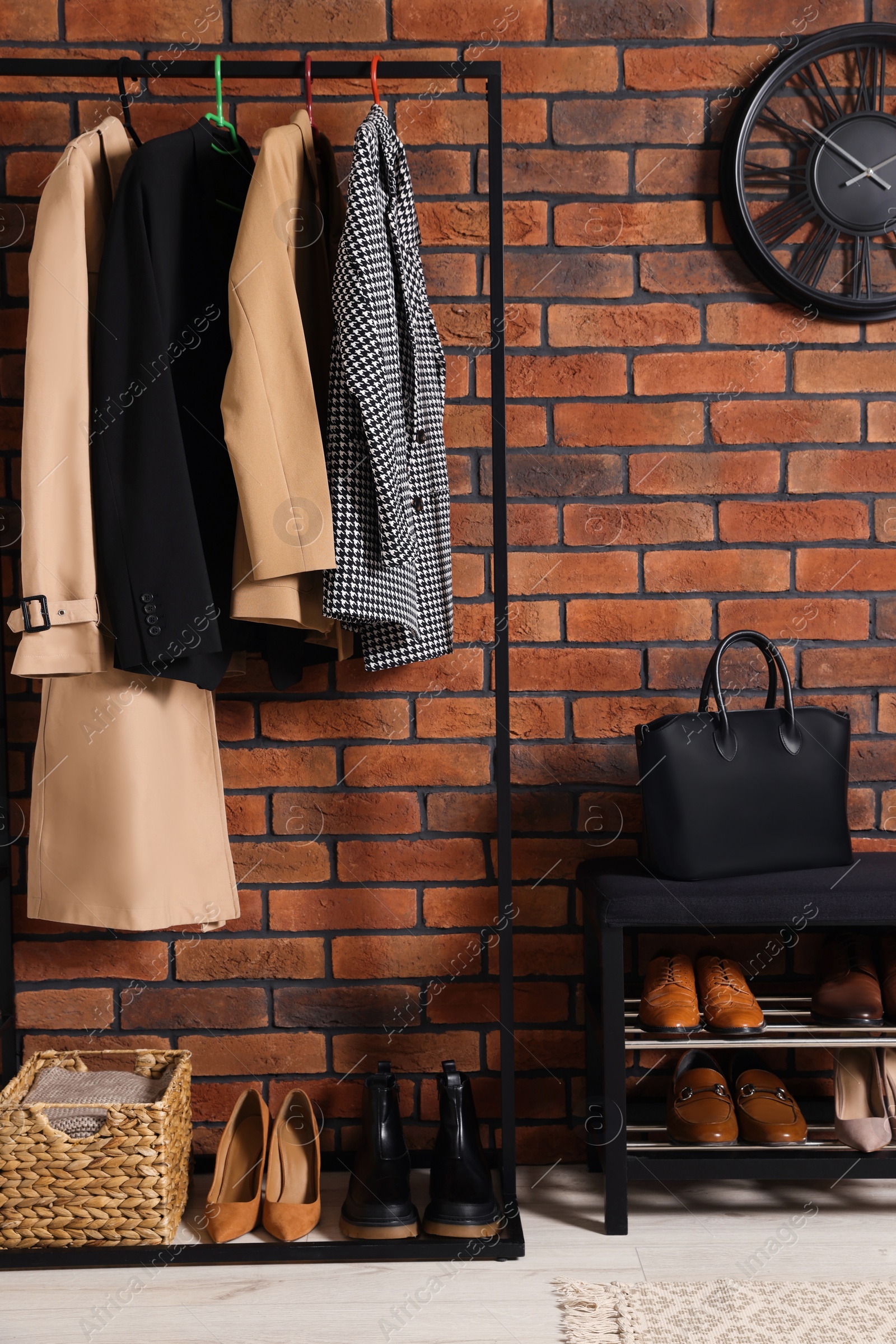 Photo of Stylish hallway with coat rack and shoe storage bench near brick wall. Interior design