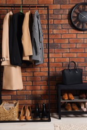 Stylish hallway with coat rack and shoe storage bench near brick wall. Interior design