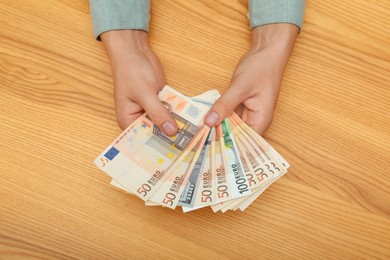 Image of Currency exchange. Woman holding euro and dollar banknotes at wooden table, closeup