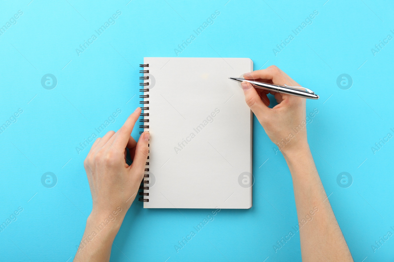 Photo of Woman writing in notebook on light blue background, top view