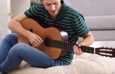 Photo of Young man playing acoustic guitar at home