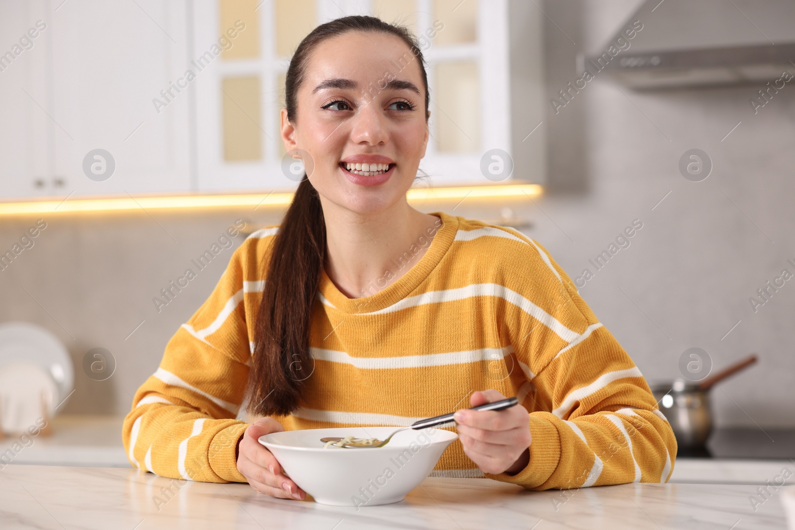 Photo of Woman eating tasty soup at white table in kitchen