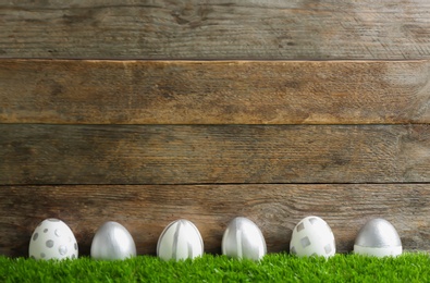Line of painted Easter eggs on green lawn against wooden background, space for text