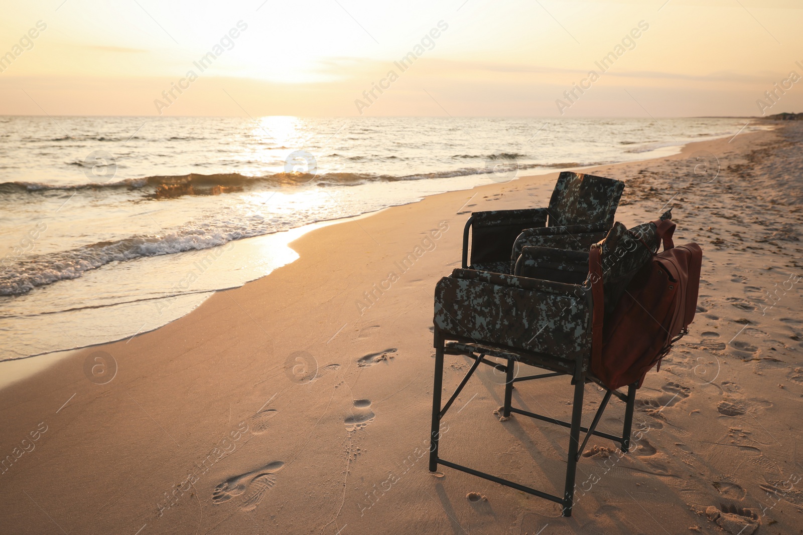 Photo of Camping chairs and backpack on sandy beach near sea, space for text