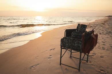 Camping chairs and backpack on sandy beach near sea, space for text