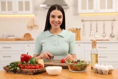 Happy woman cooking salad at table in kitchen. Keto diet